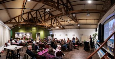 In een grote ruimte zitten ongeveer 30 mensen. Dit zijn initiatiefnemers en betrokkenen van de Landschapswerkplaats. Zij luisteren in groepjes aan tafels naar een presentatie.