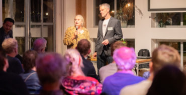 Een man en een vrouw geven een presentatie voor een publiek die naar hen kijkt.