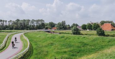 Een uitgestrekt, groen landschap met links een fietspad met een aantal fietsers en rechts een aantal vrijstaande huisjes.