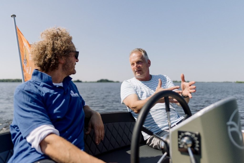 Twee mannen in gesprek op een bootje. Op de achtergrond is veel water.