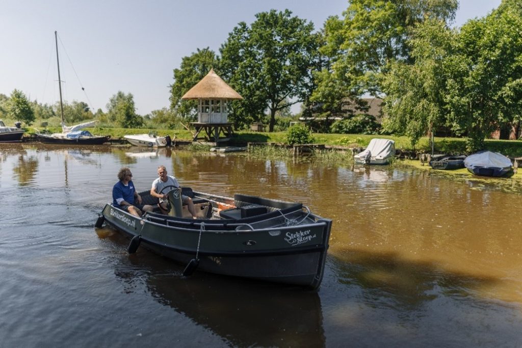 Een beeld van veraf van twee mannen op een bootje, met op de achtergrond water en natuur. 