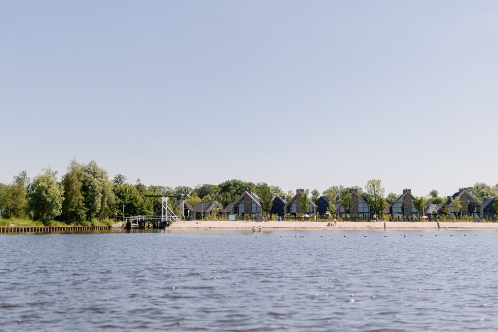 Beeld van een meer, uitlopend in een zandstrook met bomen.