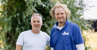 Twee mannen poseren voor de camera met op de achtergrond een boom.