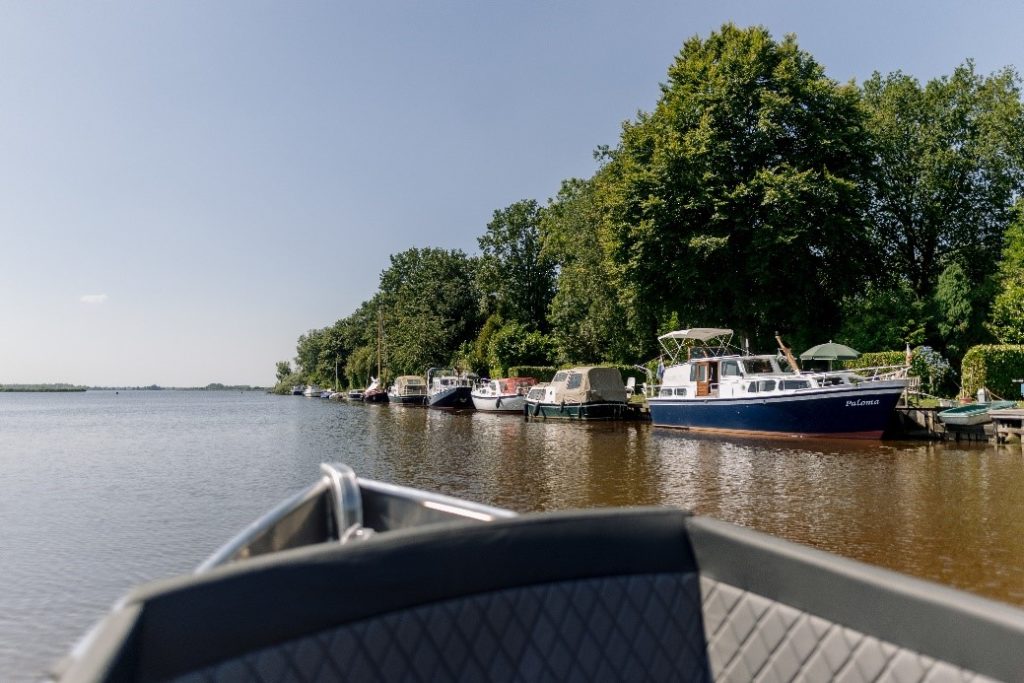 Uitzicht vanaf de voorkant van een bootje, uitkijkend over het water met rechts andere bootjes en bomen,