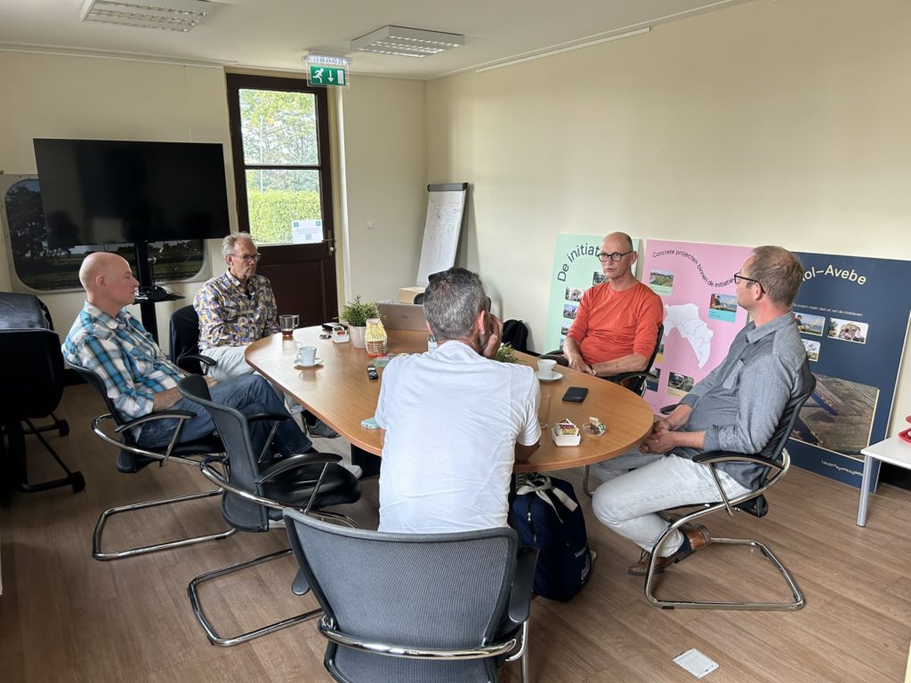 Vijf mensen zitten rond een tafel en spreken met elkaar.