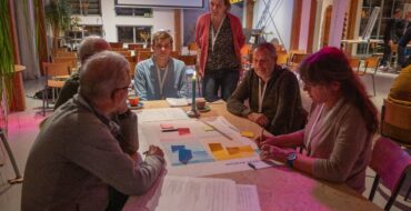 Deelnemers van een workshop aan een tafel, met papieren in het midden.