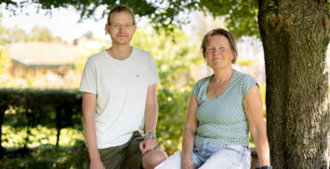 Een man links en een vrouw rechts. Zij zitten voor een groen landschap met een boom aan de rechter kant.