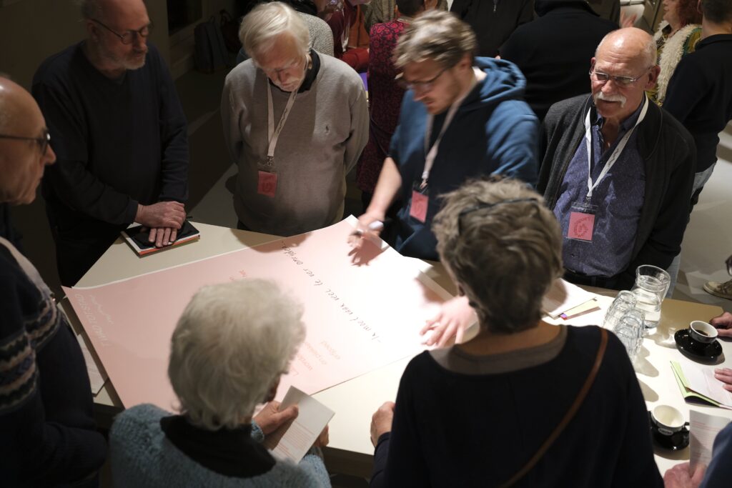 Mensen staan in een groepje rond een tafel. Hierop ligt een papier.
