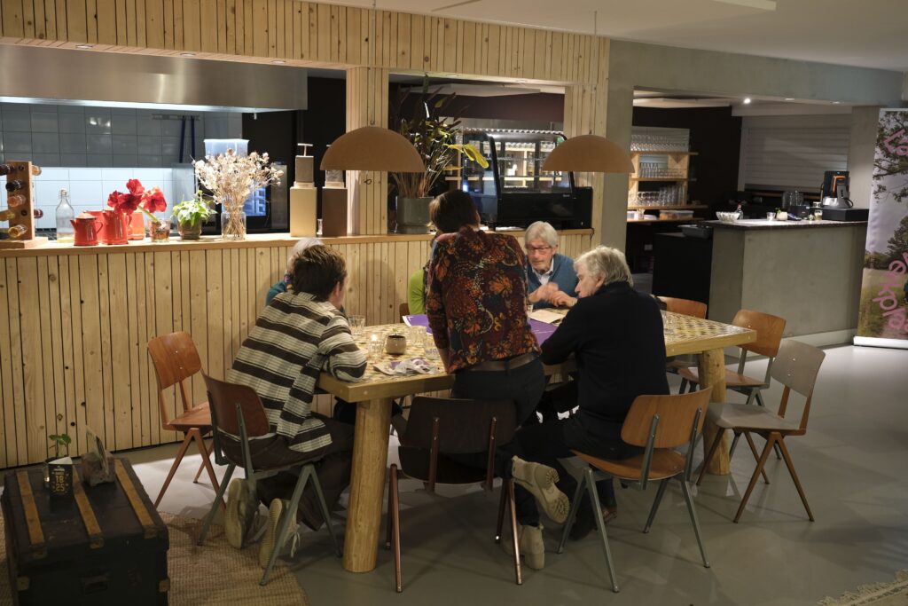 Mensen zitten in een groepje rond een tafel. Hierop ligt een papier.