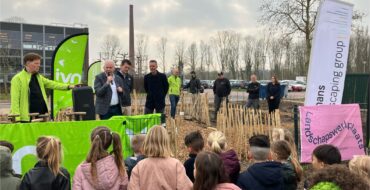 Man staat voor een groep met kleine kinderen op een schoolterrein in de buitenlucht.